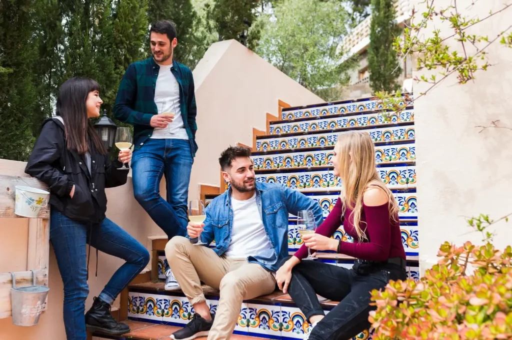 Four friends enjoying drinks and chatting on colorful, tiled outdoor stairs surrounded by greenery.